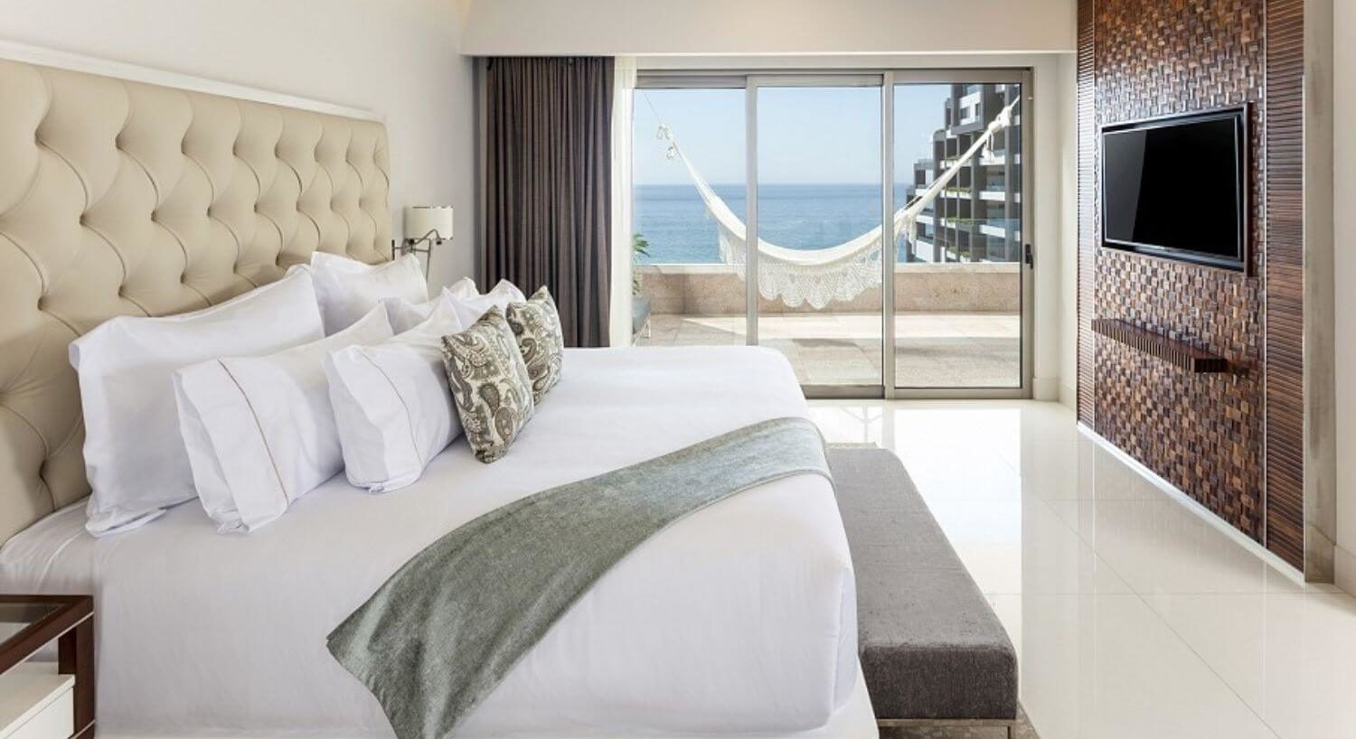 Bedroom with King bed, white bedding with sage accents, flat screen TV, and sliding doors out to a patio with hammock, ocean and resort views.