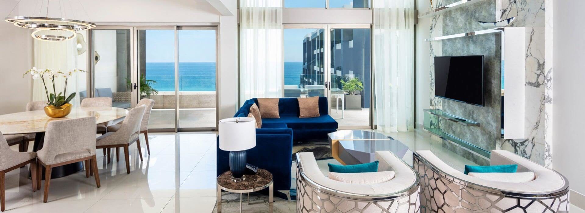 Spacious living and dining area with blue and white furniture, flat screen TV, and sliding doors out to a spacious terrace with ocean views.