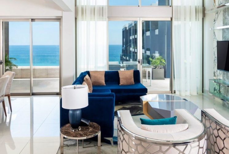 Spacious living and dining area with blue and white furniture, flat screen TV, and sliding doors out to a spacious terrace with ocean views.