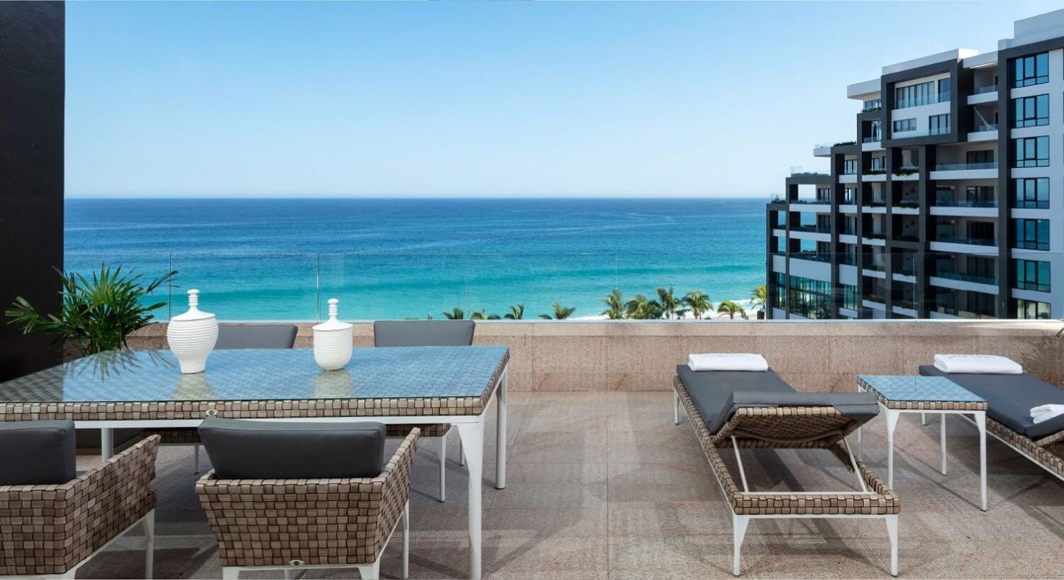 A balcony with outdoor dining table and chairs, lounge chairs, and ocean views.