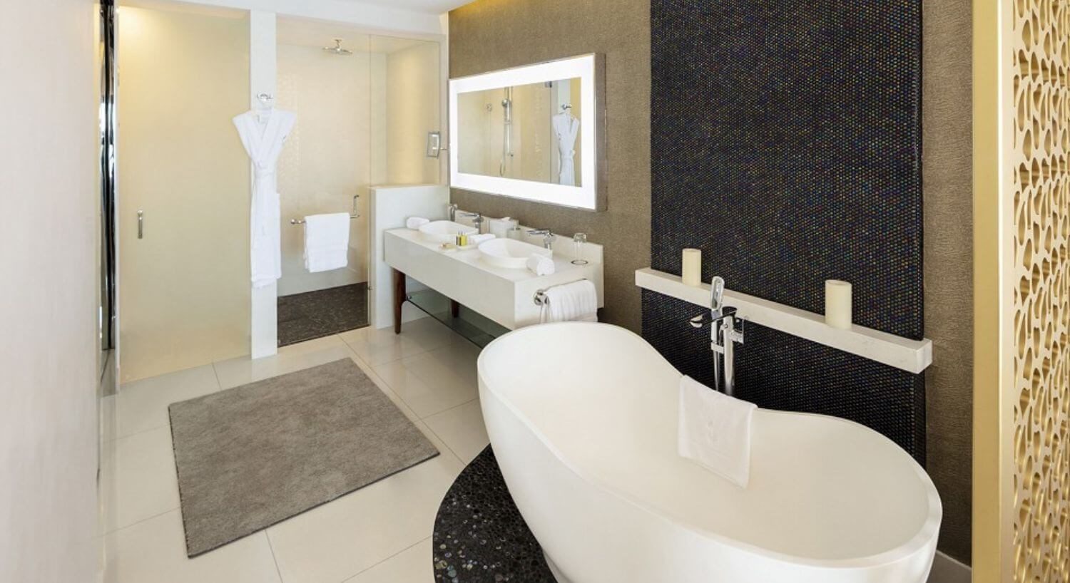 A bathroom with double sinks, a lit mirror over the sinks, a shower and separate deep soaking tub.
