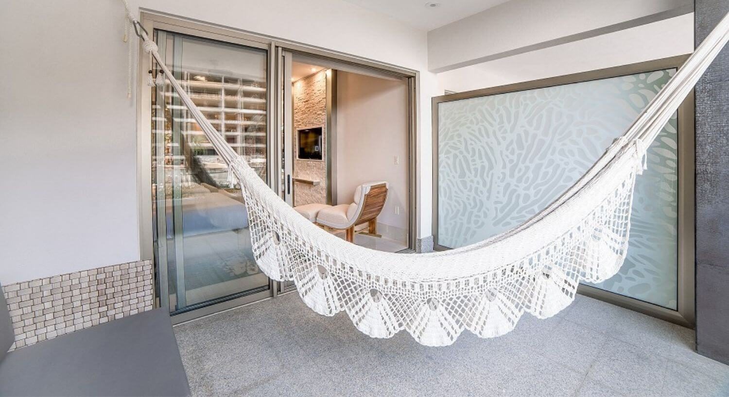 A balcony with a hammock and patio furniture, and a sliding door into a living room.