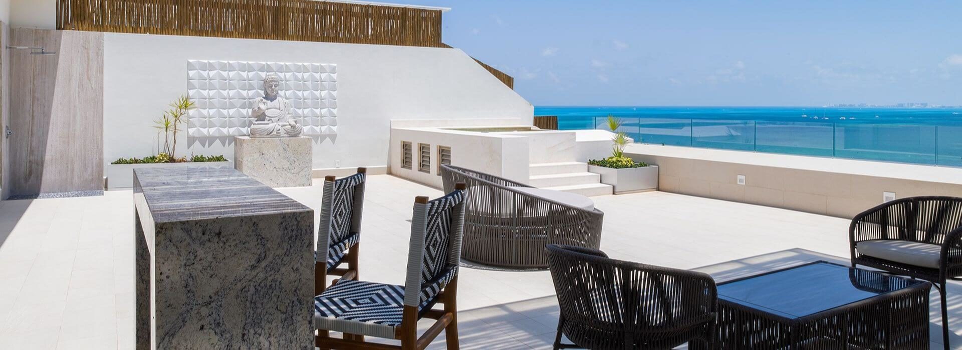 Rooftop terrace with patio furniture, lounge areas, a bar, a hot tub, and turquoise ocean views with blue skies
