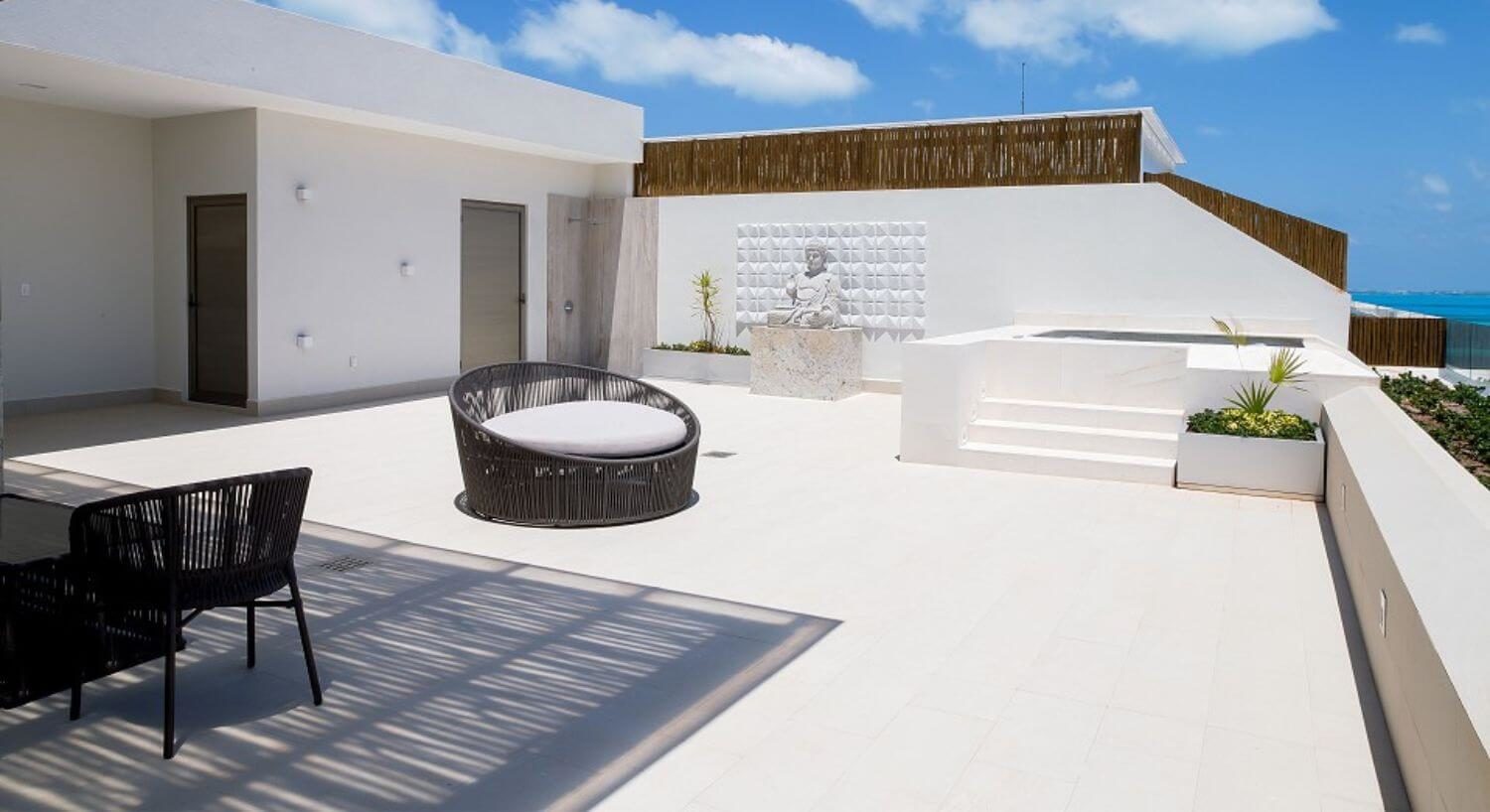 A rooftop terrace with outdoor patio furniture, a hot tub, a Buddha statue, and ocean views.