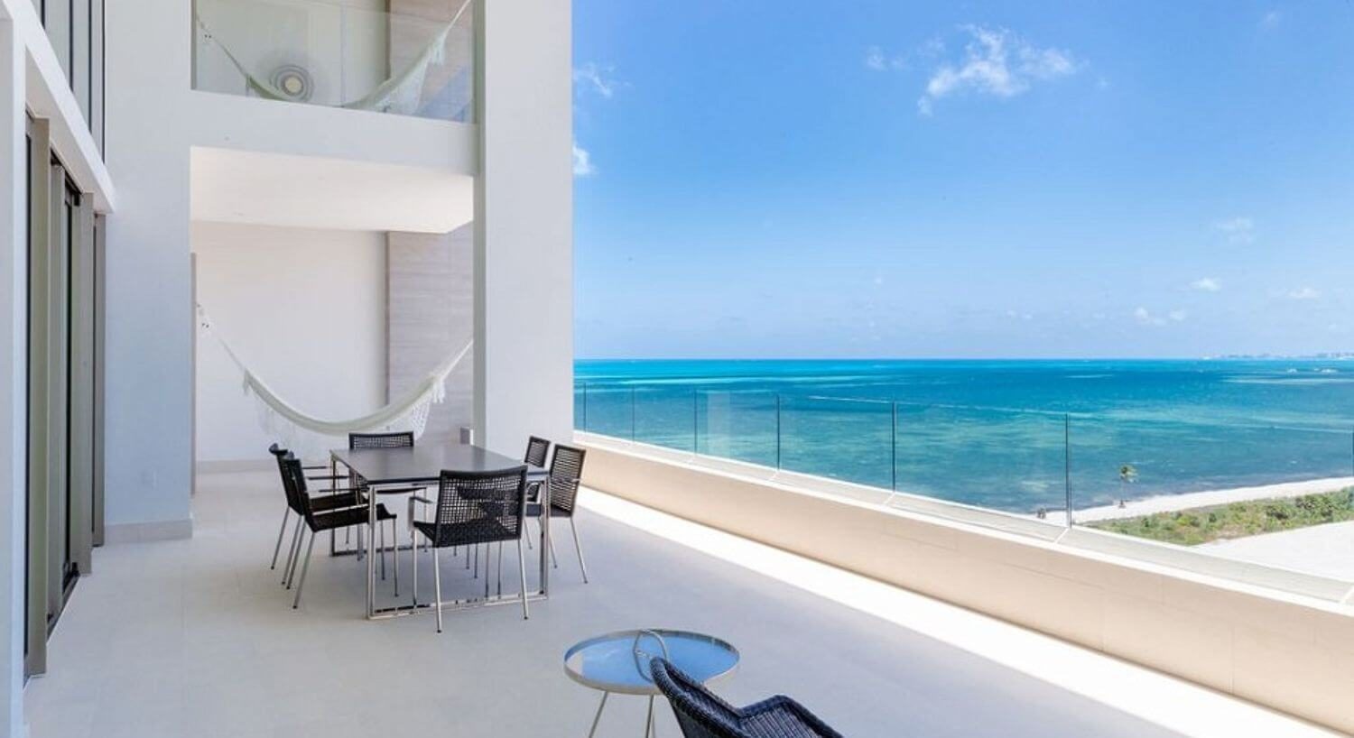 A spacious outdoor balcony with patio furniture, dining table and chairs, hammock, a second floor balcony with hammock, and sweeping views of the turquoise Caribbean ocean.