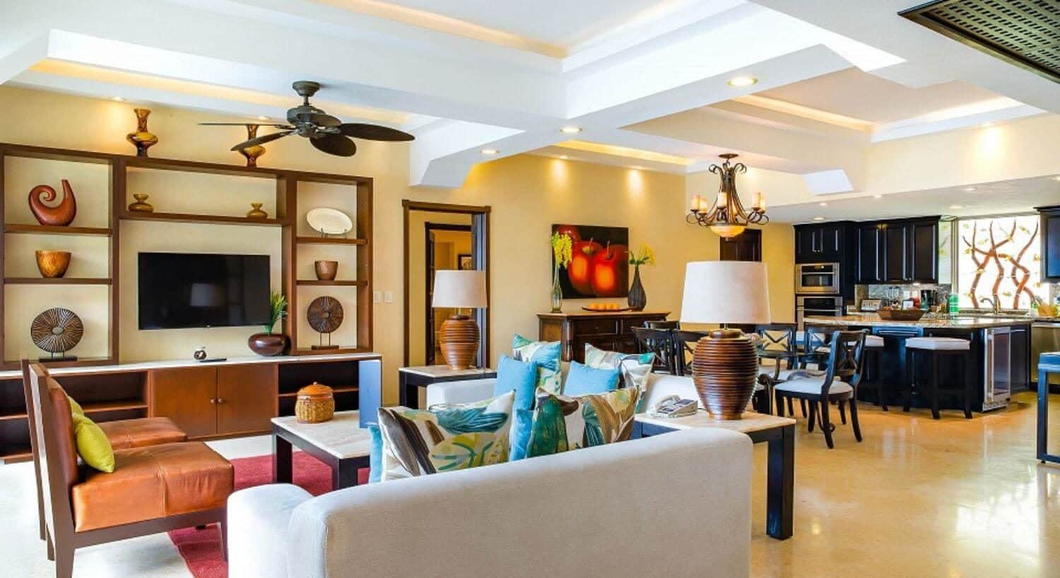 A large open room with a living area with plush white, blue and orange living furniture, a dining area, and kitchen.
