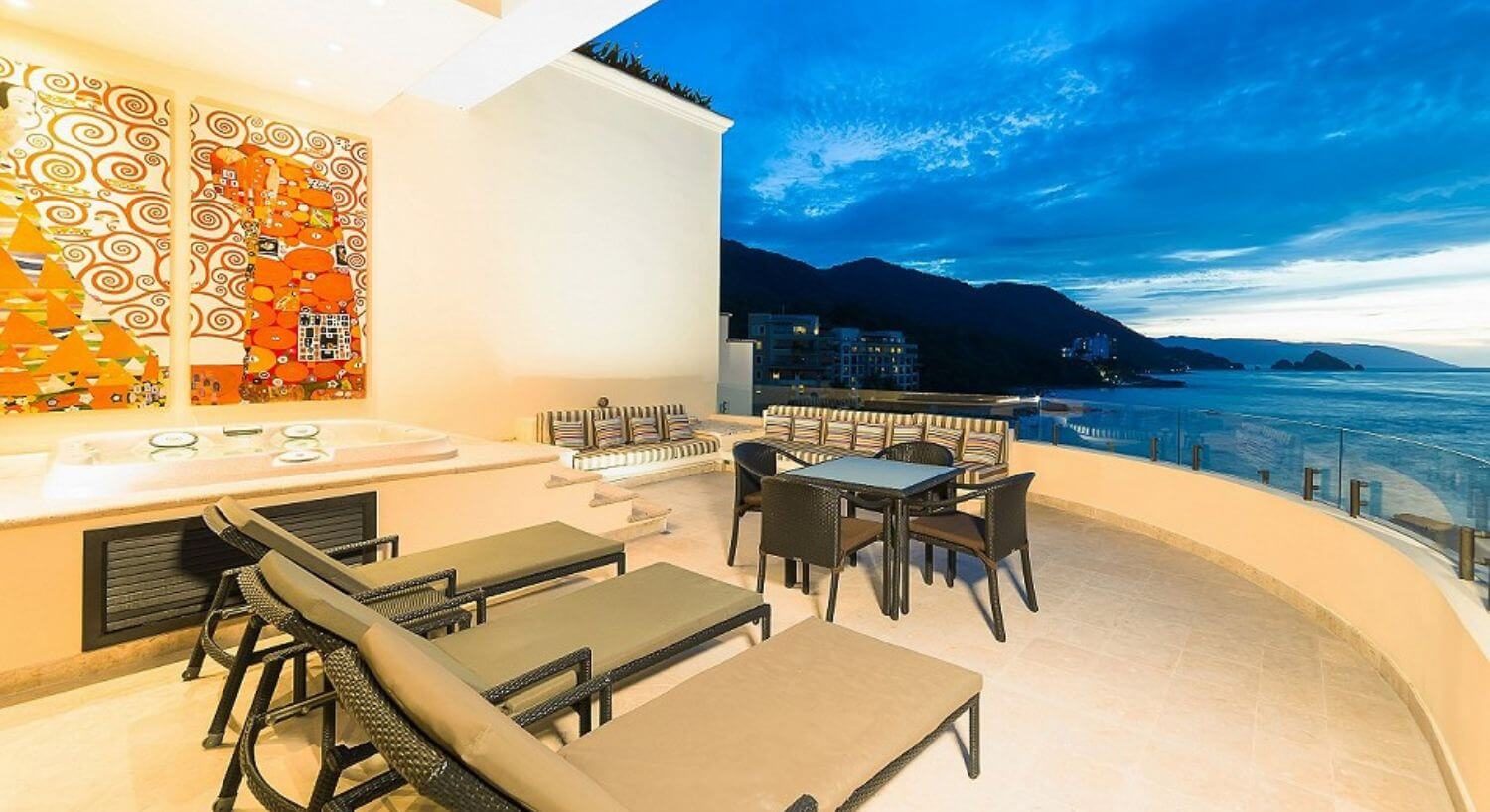 A private outdoor terrace with a hot tub, lounge chairs, table and chairs, sofas, and views of the ocean and mountains.