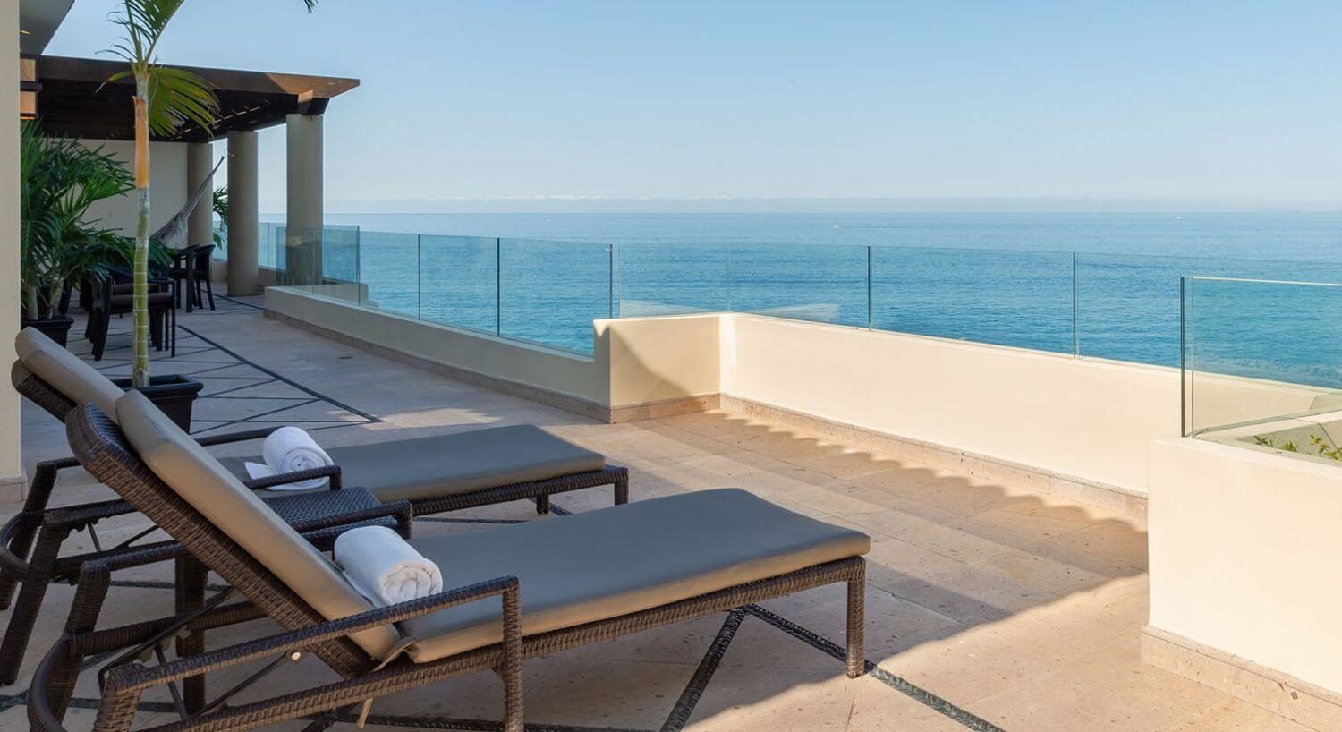 A private outdoor terrace with lounge chairs, palm trees, and stunning views of the ocean.