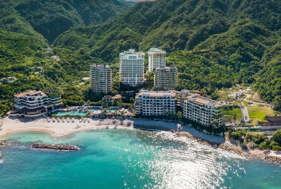 Several hotel buildings built into the side of a mountain and on the beach, with turquoise colored waters
