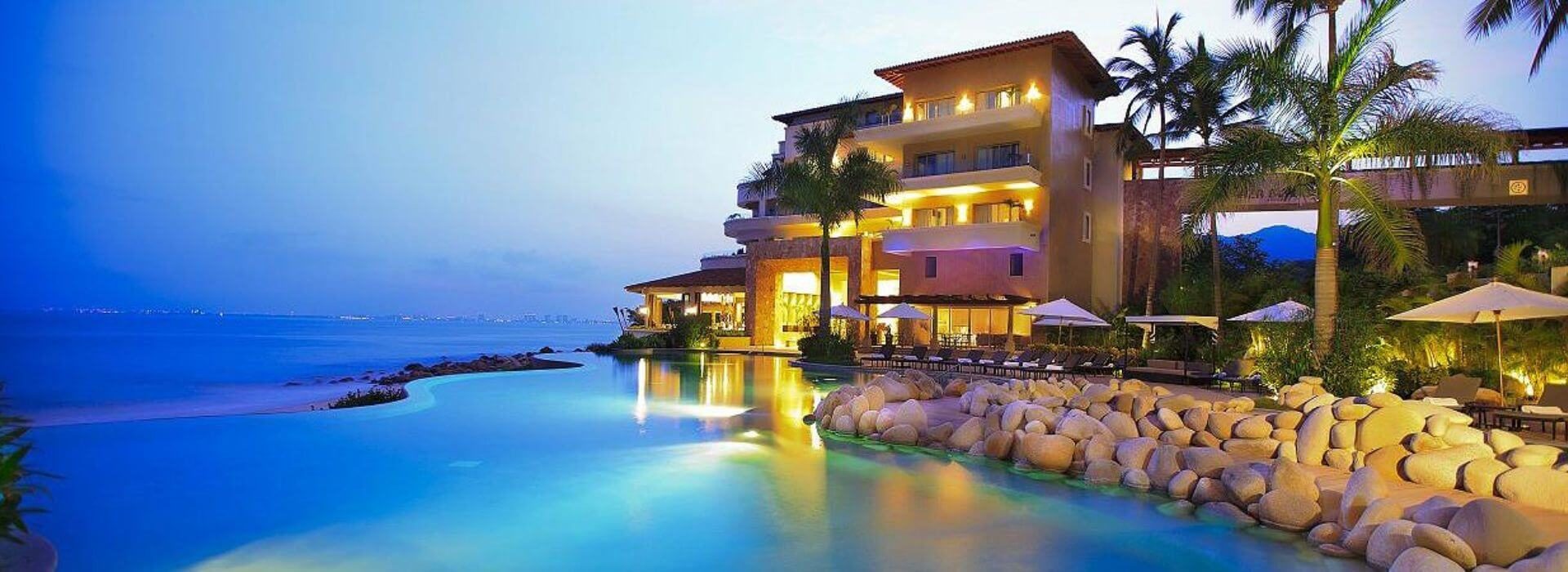A multi story villa with a pool at the bottom and the ocean in the background