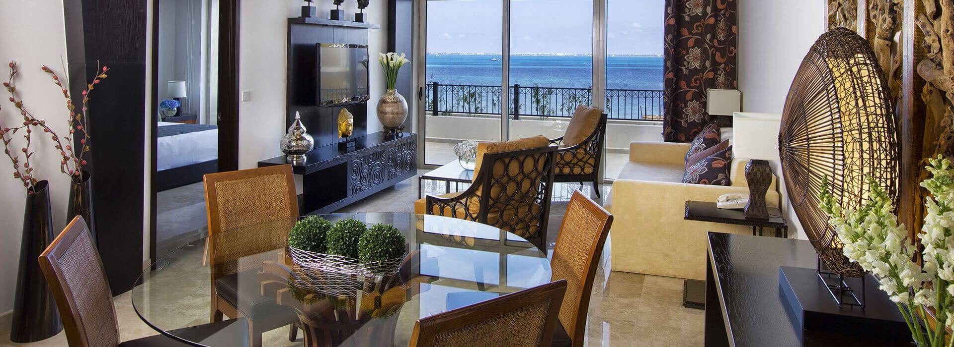 Living room and dining area with glass table, leather furniture, a flat screen TV, and sliding doors leading out to a balcony with ocean views.