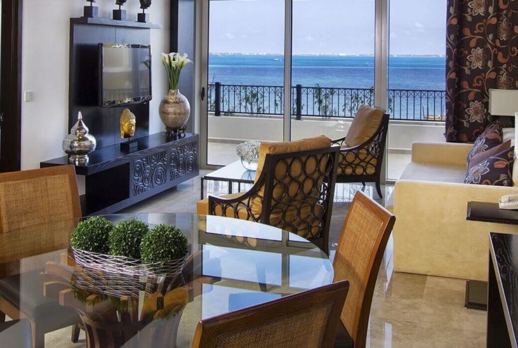 Living room and dining area with glass table, leather furniture, a flat screen TV, and sliding doors leading out to a balcony with ocean views.