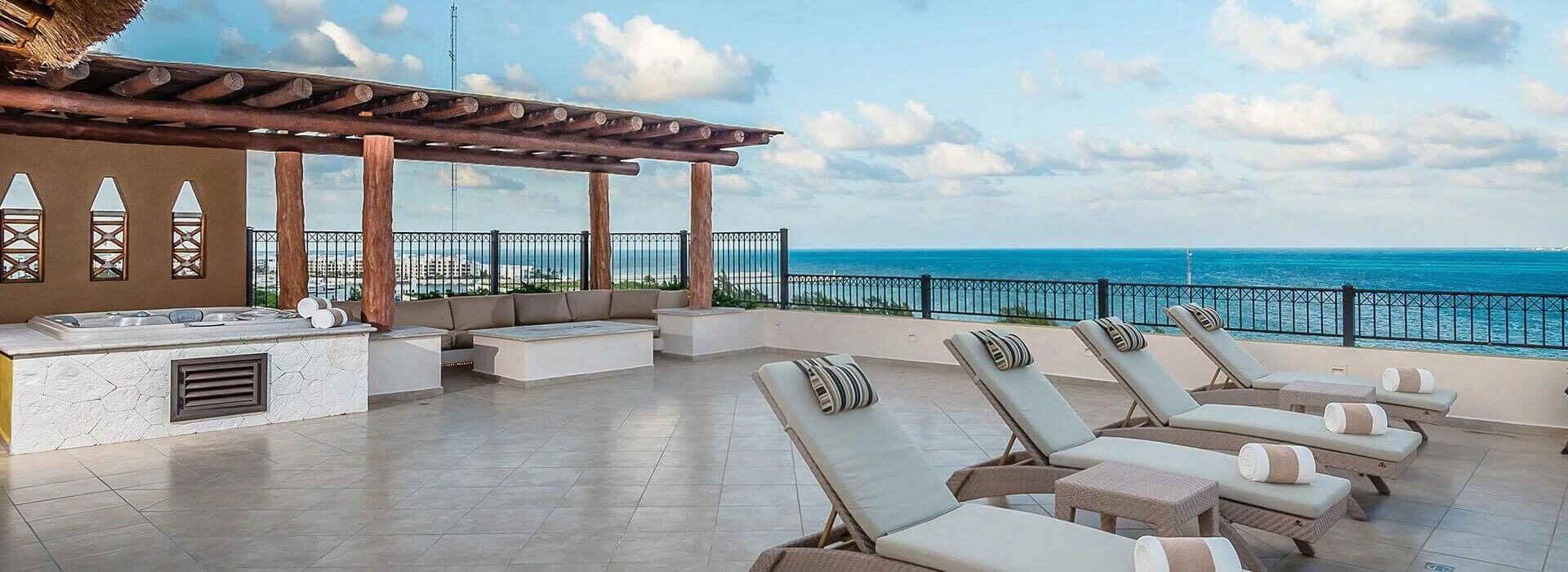 An expansive terrace with an outdoor living area with sofa, firepit, hot tub, sun loungers, and sweeping views of the turquoise Caribbean sea.
