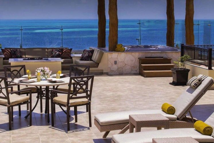 A spacious terrace with lounge chairs, a dining table and chairs, a sitting area with sofas and a fire pit, and a hot tub, and beautiful blue ocean views.