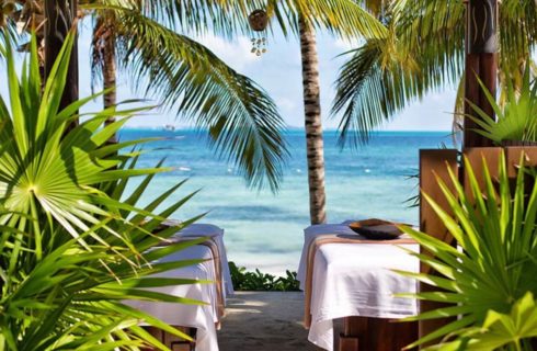 Two massage tables set up outside under palm trees facing the ocean