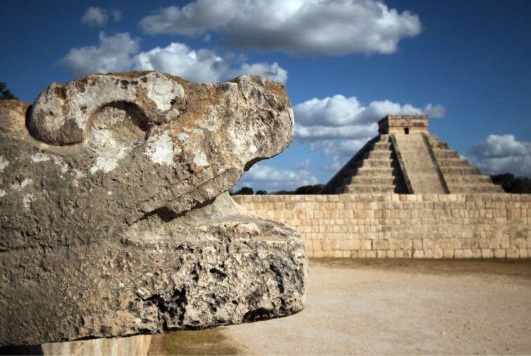 a stone snake head with a Mayan pyramid in the background
