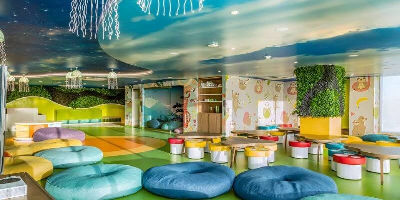 Colorful room of bean bag chairs, an under the sea mural on the ceiling, jellyfish light fixtures, and mushroom tables and chairs in a Kid's Club room.