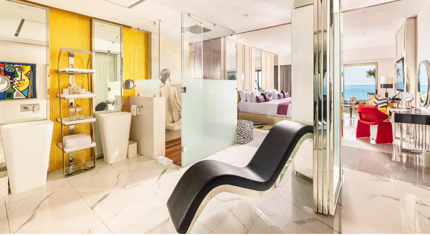 A modern hotel room with a black Tantra Chair in the foreground, leading into a bathroom and bedroom with an ocean view.