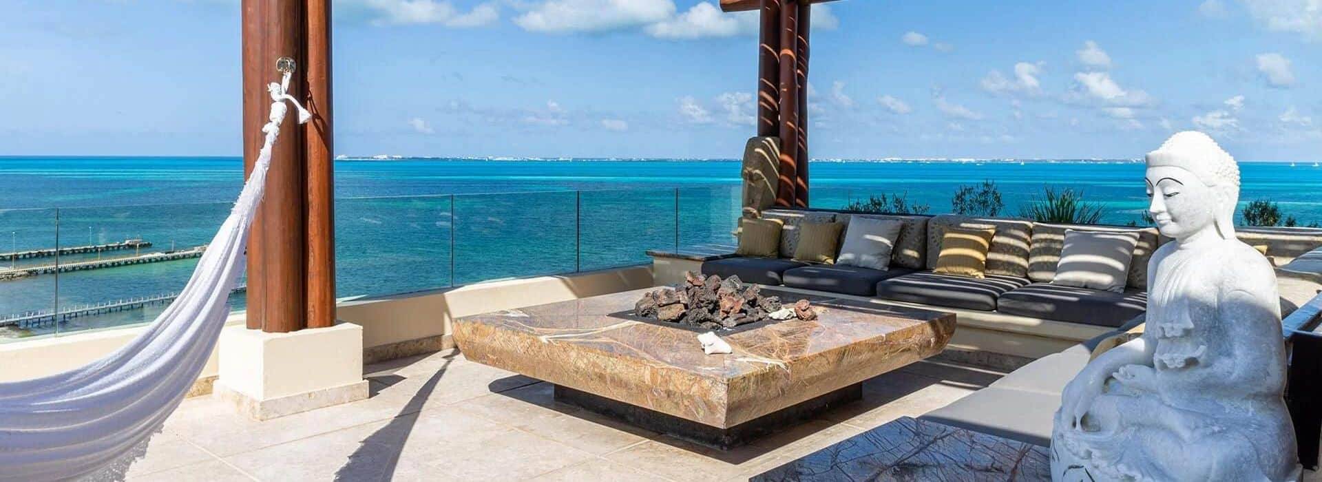 rooftop terrace with outdoor patio furniture, a firepit, a stone statue, and a background of turquoise ocean waters