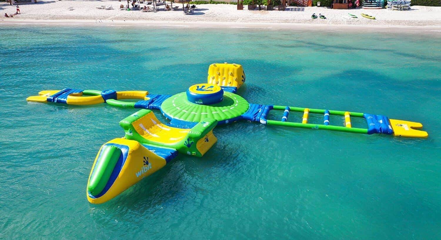 Green, yellow and blue Wibit aqua park floating in the ocean with ladders, slides, and other challenging water activities