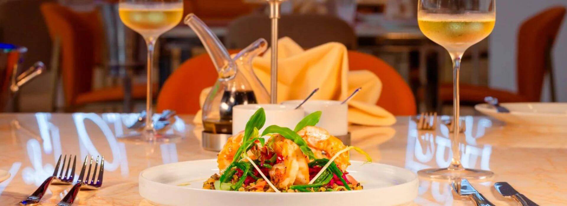 a plate of fresh shrimp and greenery with a carafe and glass of wine on the table