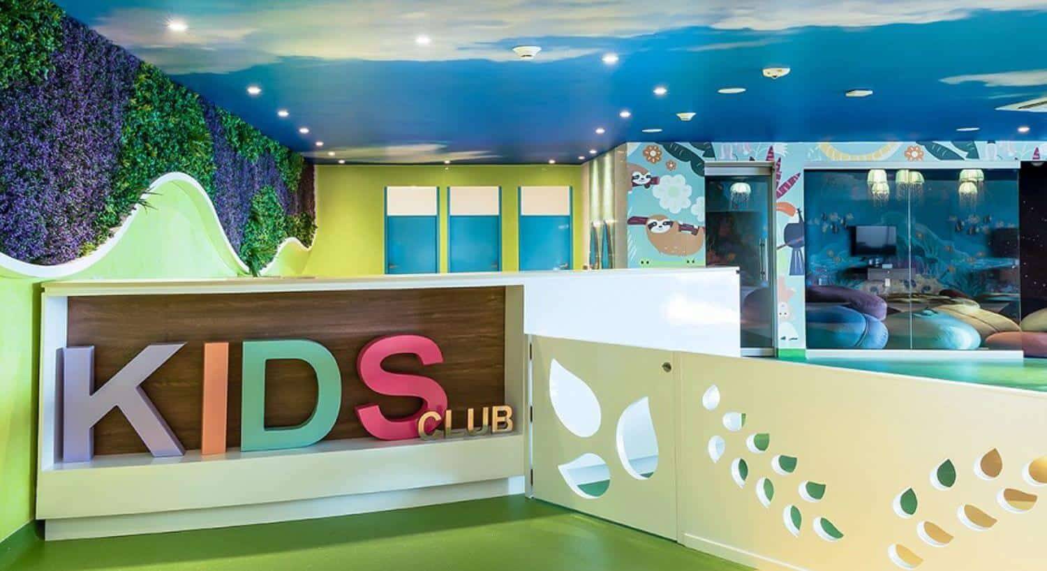 A colorful sign that says Kids Club in a room with painted walls and ceiling, and colorful activities for kids to do.
