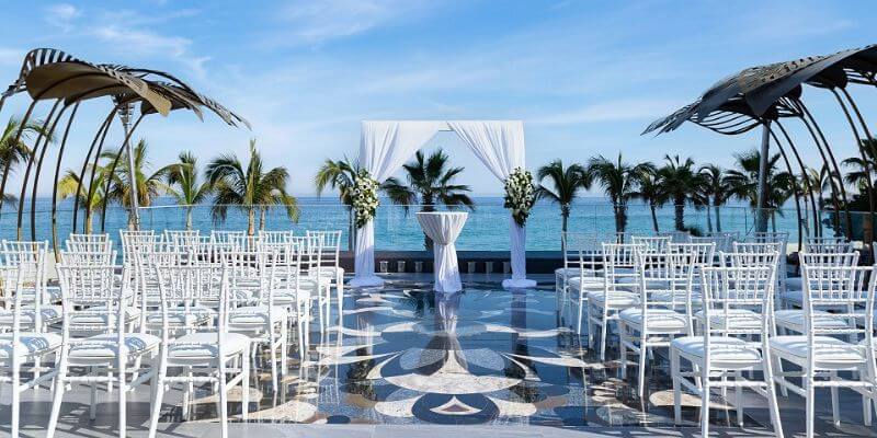 white chairs and a white canopy set up for a wedding on the beach with an ocean background